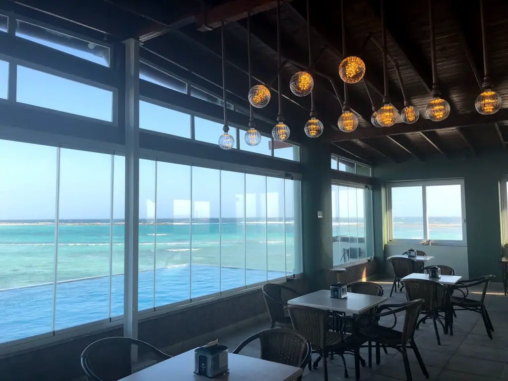 inside rum reef bar looking out windows to ocean and infinity pool aruba