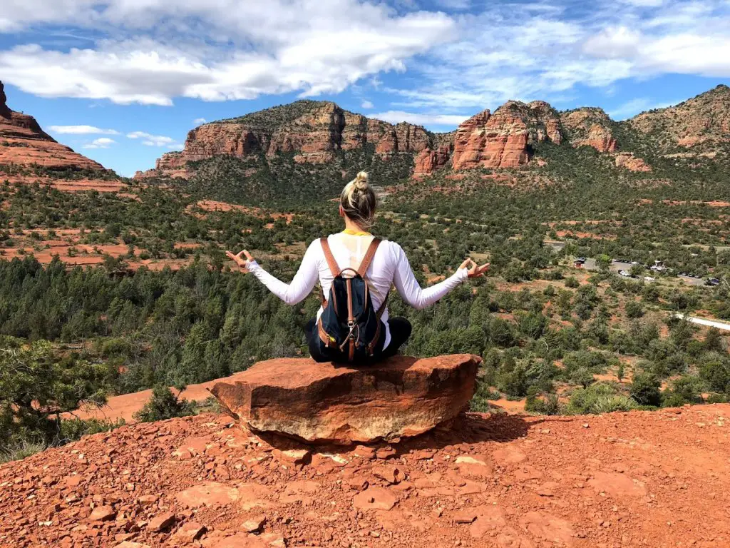 girl in meditation pose with blue backpack on red rocks ledge at bell rock